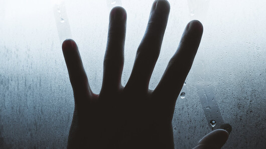 Bildet viser en hånd som holder på et vindu.