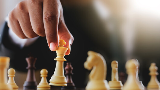 Bildet viser en dresskledd person bak et sjakkbrett med sjakkbrikker.