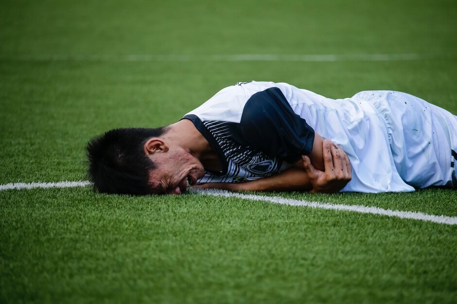 Bildet viser en fotballspiller som ligger på magen på en fotballbane. Spilleren har et fortvilt ansiktsuttrykk.