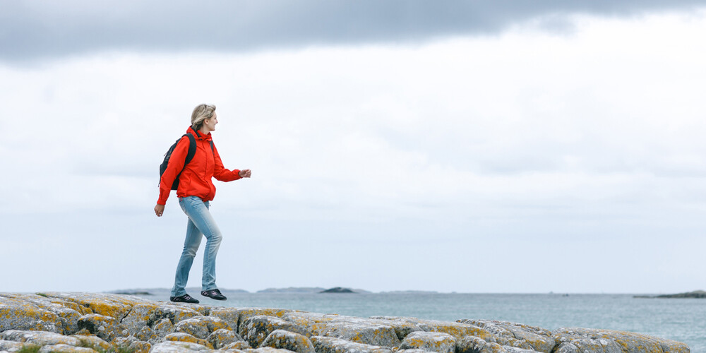 Kvinne går på svaberg langs sjøen (foto)